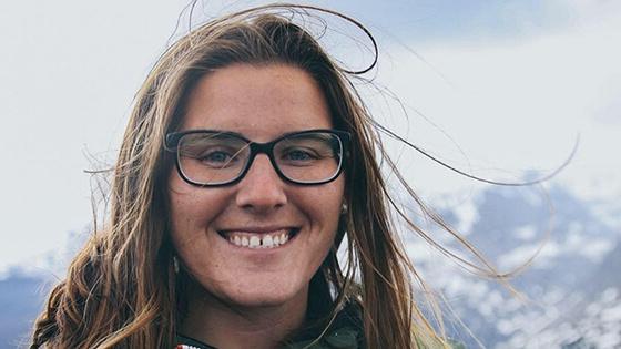满帆毕业生SaJorden Miller肩部以上的照片, 背景是白雪皑皑的山脉. 她面带微笑，穿着一件橙色的绿色拉链夹克，戴着一副黑框眼镜.